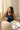 Femme assise sur un canapé, tasse à la main, portant le débardeur côtelé Martin nuit en laine mérinos et soie avec un pantalon blanc – yvo et moi