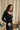 Sous-pull chaud femme en laine et soie Owen noir porté avec un jean noir, devant un rideau en lin et bouquet de fleurs – yvo et moi